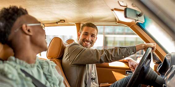 two friends smile as they go driving down the road