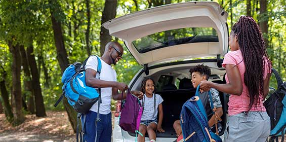 a family gathers their backpacks from the trunk of the car and go hiking