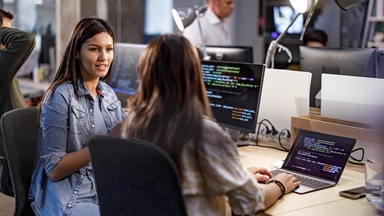 Smiling female programmer communicating with her colleague while working on computer codes in the office.